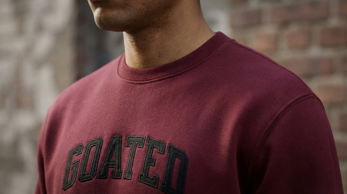 Person wearing a maroon sweatshirt with 'GOATED' text against a brick wall.